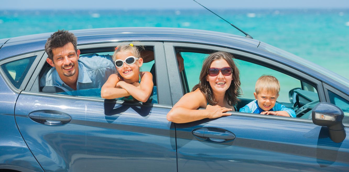 Family in a rental car beside the ocean.
